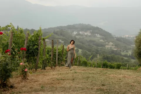 Ragazza con vestito e calice in mano passeggia tra i vigneti del Breganze DOC con le colline sullo sfondo