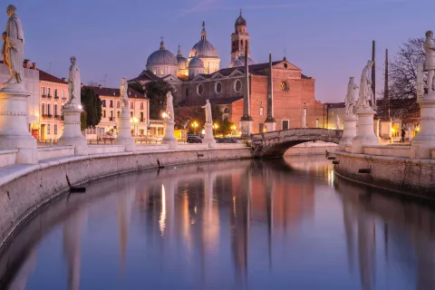 Prato della Valle a Padova illuminato al tramonto con le statue e l'Abbazia di Santa Giustina che si riflettono nell'acqua