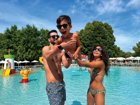 Bambino viene sollevato per gioco dalla mamma e dal papà in costume da bagno in una piscina del Parco acquatico Aquaestate a Noale