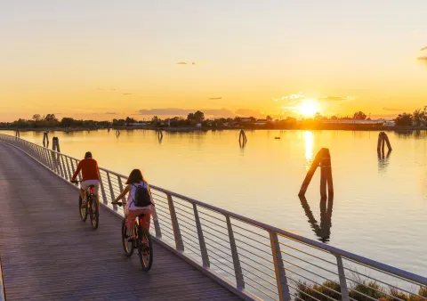 Turisti in bici sulla pista ciclabile sospesa di via Pordelio, sullo sfondo la laguna nord a Cavallino Treporti al tramonto