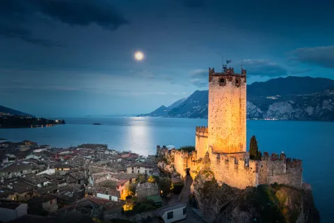 Malcesine vista dall'alto con Castello Scaligero e Lago di Garda in notturna con la luna piena