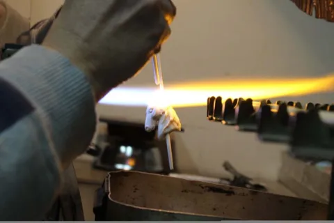 Lavorazione di una perla di vetro veneziana a forma di testa di cavallo con cannello e fiamma