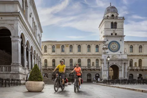 Due cicloturisti in Piazza dei Signori con la Torre dell'Orologio sulla destra a Padova