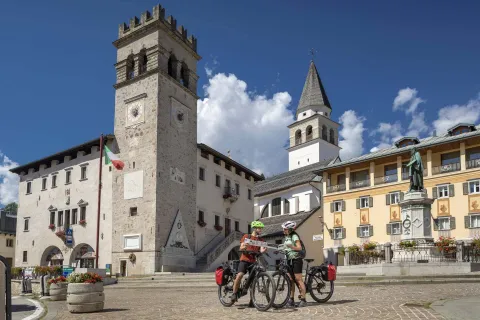 Due persone in bici che consultano mappa in Piazza TIziano a Pieve di Cadore