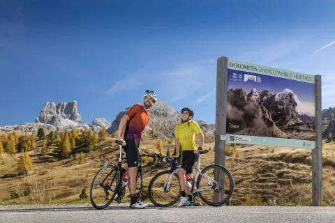 Due ciclisti osservano il paesaggio circostante fermi vicino ad un cartello sulle Tofane