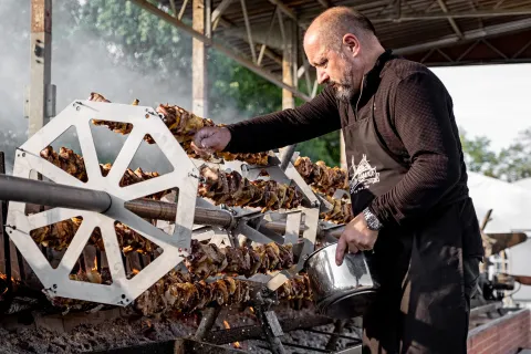 Un signore con grembiule cucina lo spiedo gigante durante una festa a Pieve di Soligo