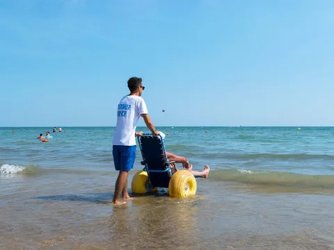 Persona accompagnata in acqua con sedia a rotelle da spiaggia a Bibione