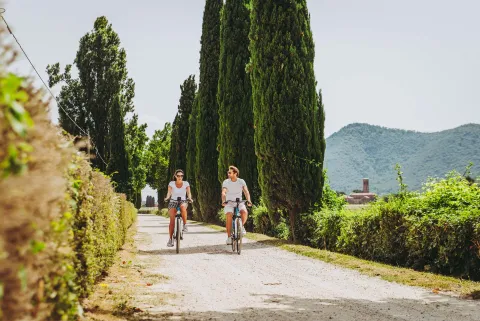 Coppia di turisti in bici su una stradina sterrata nei Colli Euganei con l'Abbazia di Praglia a Teolo sullo sfondo