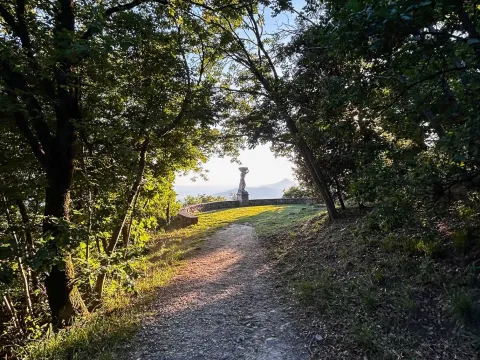 Sentiero tra il bosco sul Monte Ricco con la terrazza di Ercole e la statua che regge il mondo e sullo sfondo la sagoma dei Colli Euganei