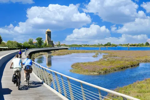 Turisti in bici sulla pista ciclabile sospesa di via Pordelio, sullo sfondo la laguna nord a Cavallino Treporti con la Torre Crepaldo