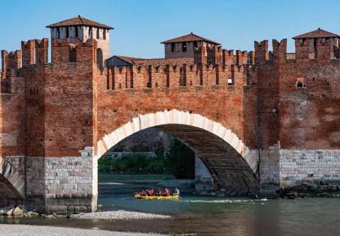 Gruppo di persone che pratica il rafting con gommone sotto il ponte di Castelvecchio a Verona
