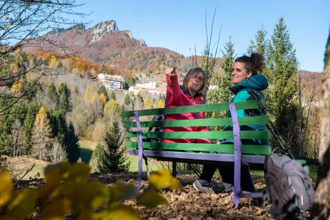 Escursioniste si riposano su una panchina davanti allo Spitz di Tonezza del Cimone in autunno con il foliage