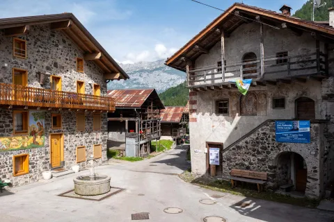 Scorcio di una piazza di Canale d'Agordo con fontana e case tradizionali in legno e pietra