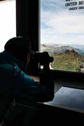 Visitatore ammira le Dolomiti con binocolo dal Museo Marmolada Grande Guerra