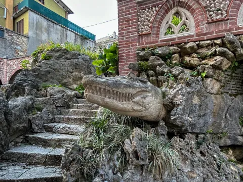 Testa di coccodrillo scolpita che emerge dalle rocce nel Giardino Jacquard Rossi di Schio